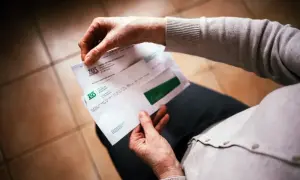 Dłoń otwiera kopertę ZUS. W środku dokumenty dotyczące 13. emerytury, być może decyzja o jej przyznaniu.
