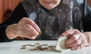 Starsza osoba liczy monety, być może czekając na rentę chorobową. Dłonie z widocznymi zmarszczkami układają drobne pieniądze obok portmonetki.