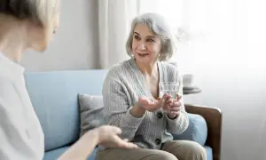 Starsza pani z niepełnosprawnością bierze leki, otrzymując pomoc od opiekunki.