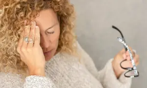 Kobieta z kręconymi włosami masuje skroń, czując się przygnębiona. Czy to mogą być objawy psychiczne helicobacter pylori?