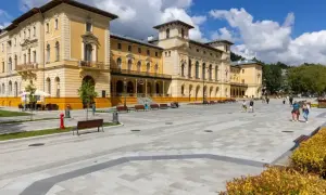 Elegancki budynek sanatorium, plac z ławkami i spacerujący ludzie. Dowiedz się o nowe zasady wyjazdu do sanatorium na NFZ.
