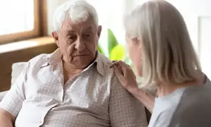 Starszy mężczyzna z fobią społeczną, smutny, z ręką kobiety na ramieniu.