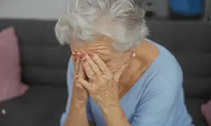 Starsza kobieta z siwymi włosami zakrywa twarz dłońmi, być może doświadczając trudnych emocji związanych z objawami alzheimera.