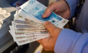 Dłonie trzymają stos polskich banknotów, symbolizujących waloryzację emerytury. Widać nominały 50, 100 i 200 zł.