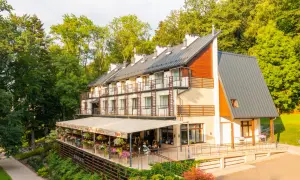Nowoczesny budynek sanatorium z tarasem i restauracją, otoczony zielenią.