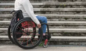 Osoba na wózku inwalidzkim, z umiarkowanym stopniem niepełnosprawności, próbuje pokonać schody.