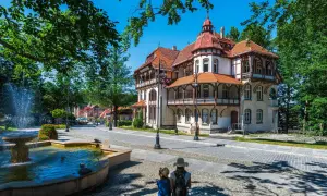 Architektura sanatorium z fontanną i dwoma osobami patrzącymi w stronę budynku.