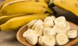 Kawałki dojrzałego banana w drewnianej miseczce, obok całe owoce.