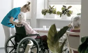 Opiekunka pomaga starszej kobiecie na wózku inwalidzkim. To przykład troski w geriatrii, która zajmuje się zdrowiem seniorów.
