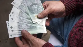 Dłonie seniora trzymają stos banknotów 100 zł. To może być pomoc z programu 800 plus dla seniorów.