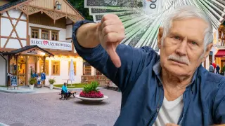 Starszy pan pokazuje kciuk w dół, trzymając stos banknotów. W tle budynek "Serce Uzdrowiska" w Szczawnicy.