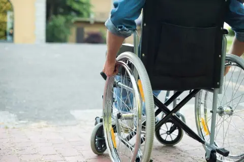 Osoba na wózku inwalidzkim, która może skorzystać z programu 500 plus dla niepełnosprawnych, porusza się po chodniku.