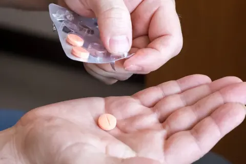 Dłoń przyjmuje pomarańczową tabletkę na cholesterol z blistra.