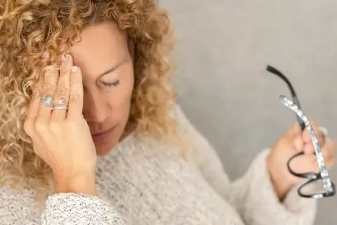 Kobieta z kręconymi włosami masuje skroń, czując się przygnębiona. Czy to mogą być objawy psychiczne helicobacter pylori?