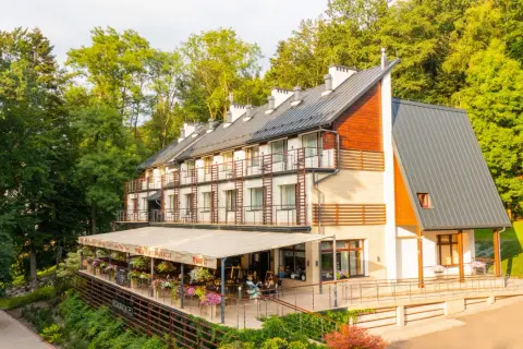 Nowoczesny budynek sanatorium z tarasem i restauracją, otoczony zielenią.