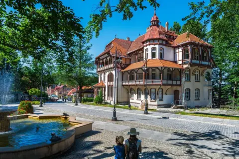 Architektura sanatorium z fontanną i dwoma osobami patrzącymi w stronę budynku.