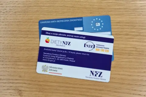 Europejska karta ubezpieczenia zdrowotnego i karta DIETYNFZ leżą na drewnianym blacie.