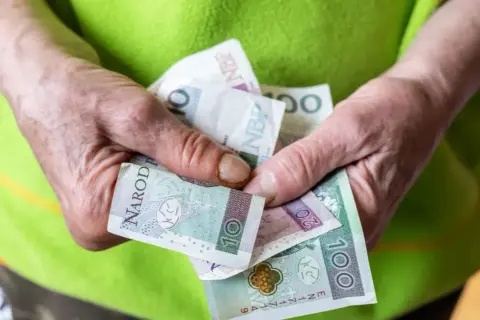 Dłonie trzymają polskie banknoty: 10, 20 i 100 zł. Zastanawiasz się, ile wynosi renta socjalna?