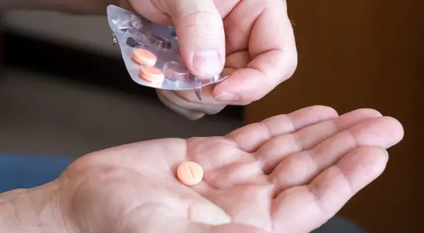 Dłoń przyjmuje pomarańczową tabletkę na cholesterol z blistra.