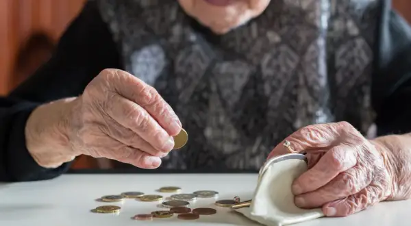 Starsza osoba liczy monety, być może czekając na rentę chorobową. Dłonie z widocznymi zmarszczkami układają drobne pieniądze obok portmonetki.