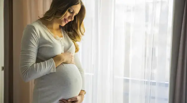 Uśmiechnięta ciężarna kobieta trzymająca się za brzuch. Czas na aspargin na co? Na zdrowie mamy i dziecka.
