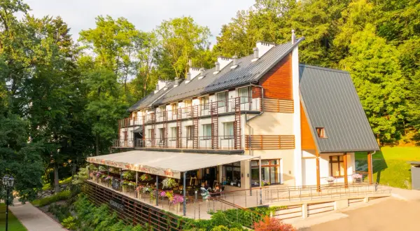Nowoczesny budynek sanatorium z tarasem i restauracją, otoczony zielenią.