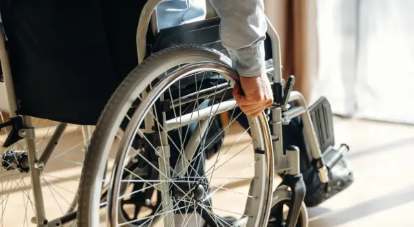Osoba w wózku inwalidzkim chwyta za koło. Orzeczenie o niepełnosprawności otwiera drogę do wsparcia i możliwości.