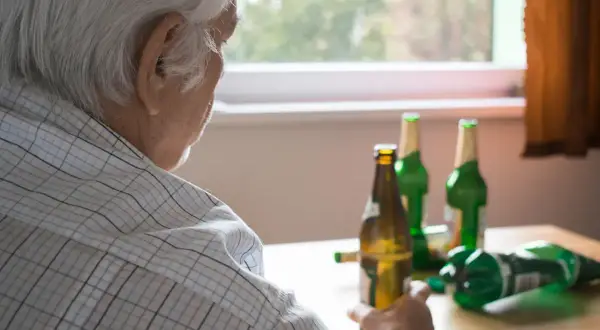 Starszy mężczyzna zmagający się z alkoholizmem, siedzi przy stole z kilkoma pustymi butelkami po piwie.