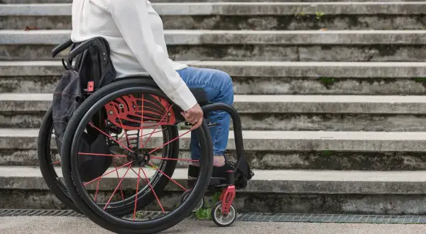 Osoba na wózku inwalidzkim, z umiarkowanym stopniem niepełnosprawności, próbuje pokonać schody.