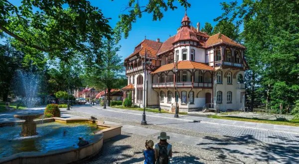 Architektura sanatorium z fontanną i dwoma osobami patrzącymi w stronę budynku.