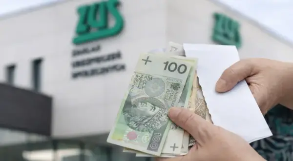 Ręce trzymają polskie banknoty przed budynkiem ZUS. Wypłata 14 emerytury wreszcie nadeszła.