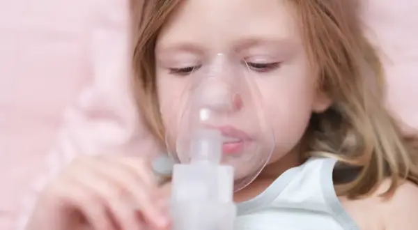 Mała dziewczynka z maską inhalatora na twarzy. Pomaga jej to w leczeniu kaszlu.