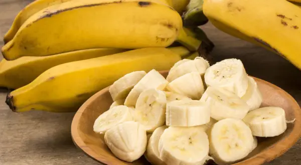Kawałki dojrzałego banana w drewnianej miseczce, obok całe owoce.