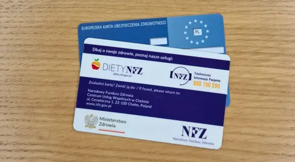 Europejska karta ubezpieczenia zdrowotnego i karta DIETYNFZ leżą na drewnianym blacie.