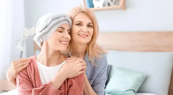 Dwie kobiety, jedna w chuście na głowie, uśmiechają się do siebie. Wsparcie i nadzieja w trudnych chwilach, gdy liczy się leczenie paliatywne.
