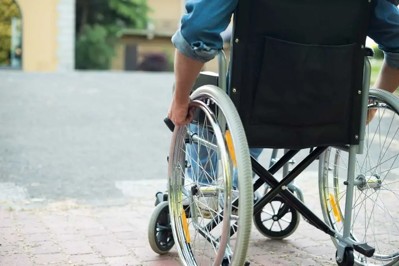 Osoba na wózku inwalidzkim, która może skorzystać z programu 500 plus dla niepełnosprawnych, porusza się po chodniku.