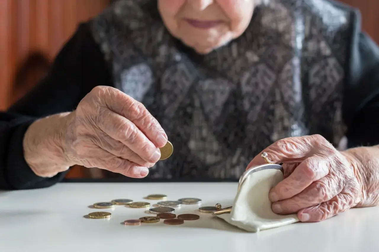 Starsza osoba liczy monety, być może czekając na rentę chorobową. Dłonie z widocznymi zmarszczkami układają drobne pieniądze obok portmonetki.