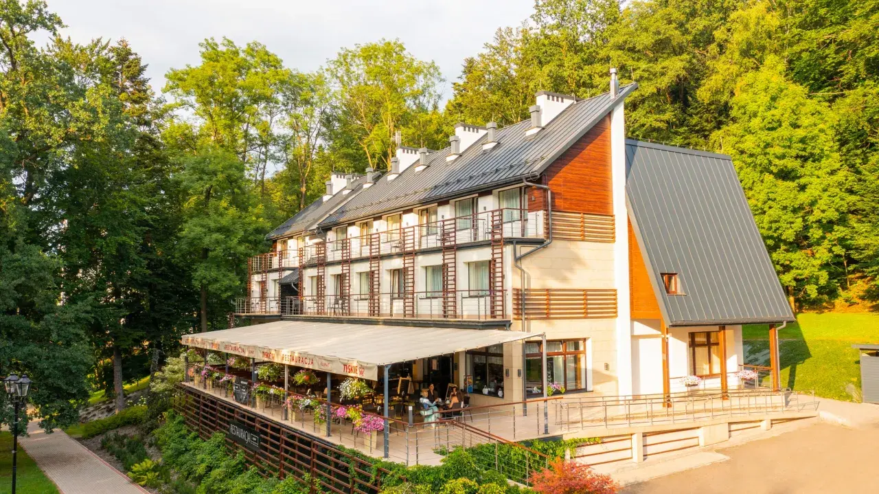 Nowoczesny budynek sanatorium z tarasem i restauracją, otoczony zielenią.