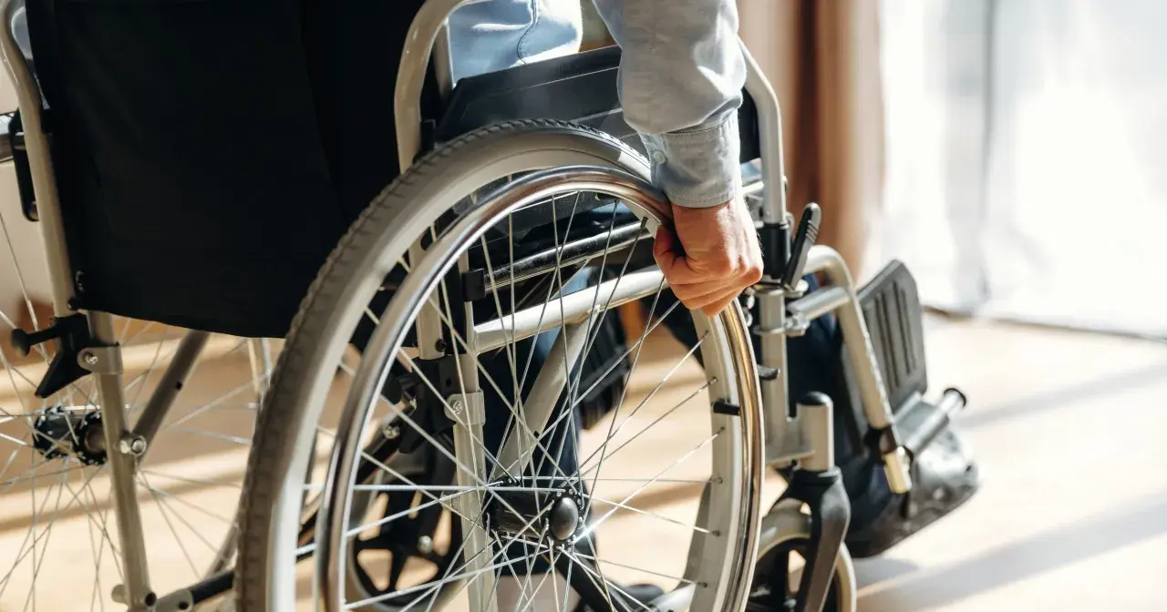 Osoba w wózku inwalidzkim chwyta za koło. Orzeczenie o niepełnosprawności otwiera drogę do wsparcia i możliwości.