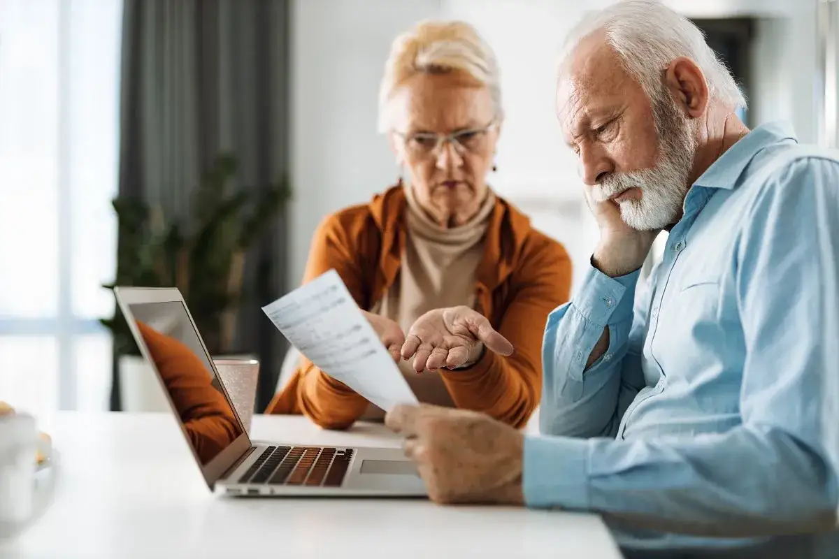Zmartwieni seniorzy analizują rachunki przy laptopie. Czy trzynasta emerytura wystarczy na pokrycie wszystkich wydatków?