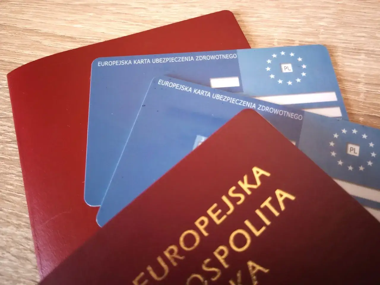 Czerwony paszport i dwie niebieskie karty, na których widnieje napis
