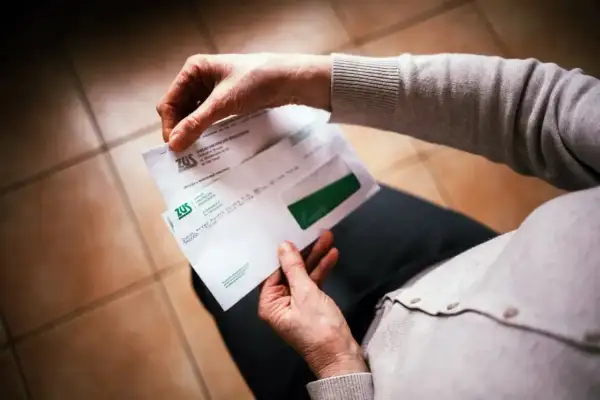 Dłoń otwiera kopertę ZUS. W środku dokumenty dotyczące 13. emerytury, być może decyzja o jej przyznaniu.