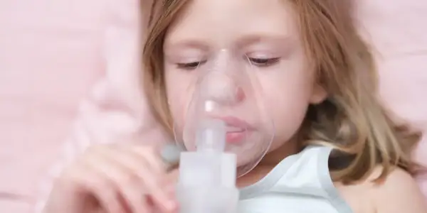 Mała dziewczynka z maską inhalatora na twarzy. Pomaga jej to w leczeniu kaszlu.