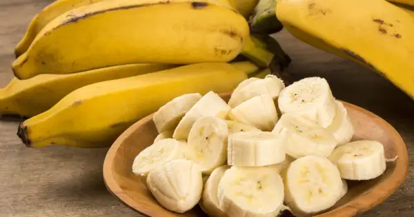 Kawałki dojrzałego banana w drewnianej miseczce, obok całe owoce.
